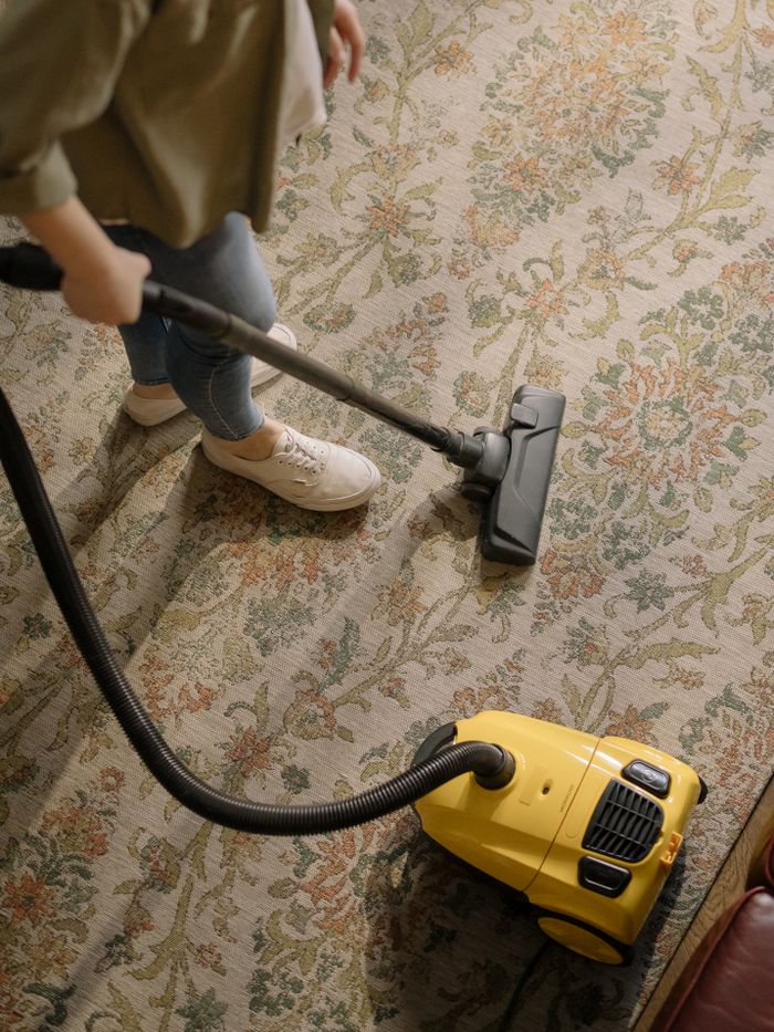 creative-03 Person nettoyant un tapis floral avec un aspirateur jaune à l’intérieur.